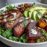 Freshly assembled butternut squash steak bowls show tender squash cubes, juicy steak strips, vibrant greens, and red onion, sprinkled with toasted pepitas.