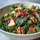 The Kale and Pomegranate Bowl showcases tender massaged kale with bright ruby seeds, sweet apples, and hearty walnuts, served on a rustic plate.