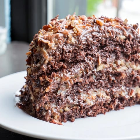 A slice of German chocolate cake displays fluffy frosting loaded with pecans and coconut on a plate.