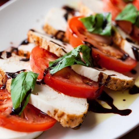 A close-up of juicy grilled chicken atop fresh Caprese salad with basil and balsamic drizzle.