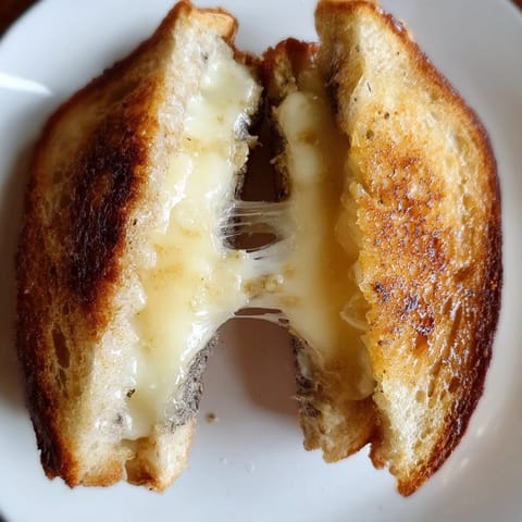 Two halves of a Truffle Grilled Cheese sandwich revealing gooey, melted Gruyère and a drizzle of black truffle oil.
