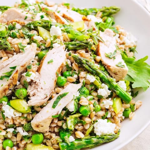 Overhead view of Warm Spring Farro Chicken Salad featuring chopped chicken, farro, crisp asparagus, peas, and arugula drizzled with zesty lemon dressing.