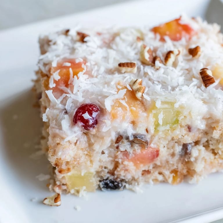 Warm fruit cocktail cake picture with visible fruit pieces, topped with creamy, sweet coconut frosting.