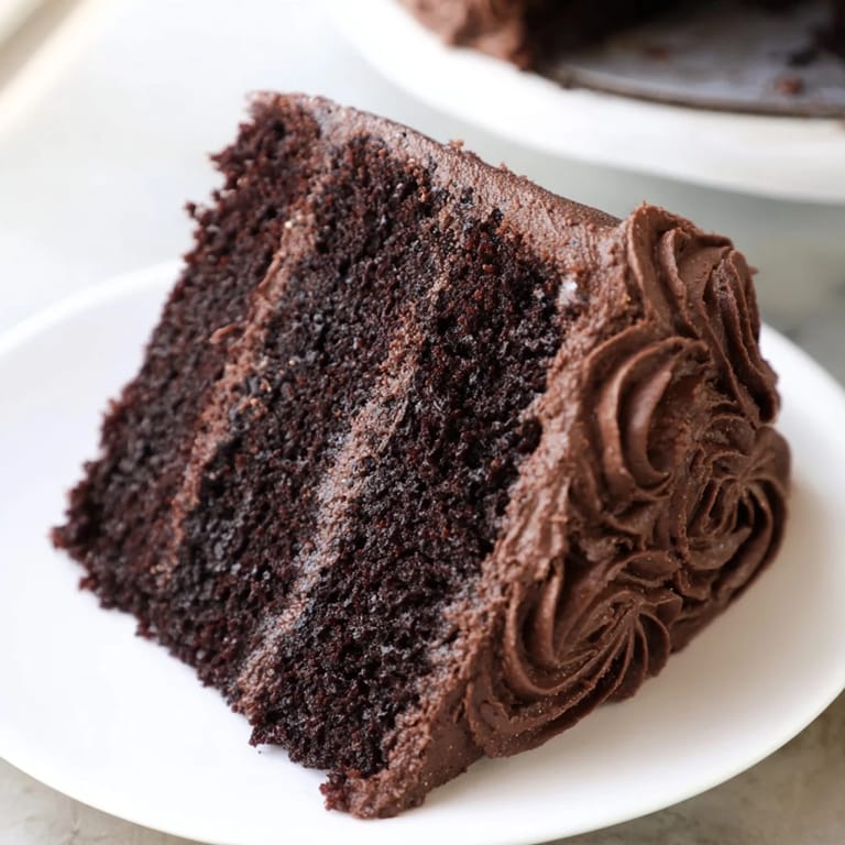 Rich, dark, layered Devils Food Cake, frosted generously and ready for serving with a fork.