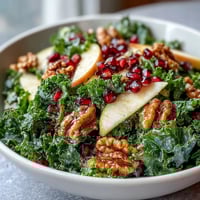 Fresh kale salad with vibrant pomegranate seeds, crisp apple slices, and crunchy walnuts tossed in a tangy apple cider vinaigrette.